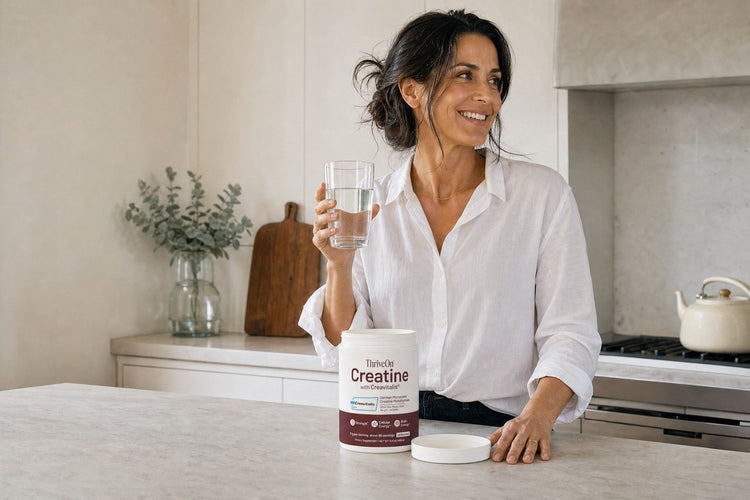 ThriveOn Creatine with Creavitalis® on a kitchen counter beside a woman holding a glass of water