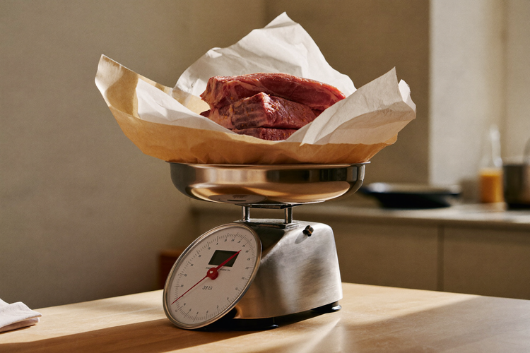 A kitchen scale stacked with raw steaks wrapped in butcher paper, the roughly two and a half pounds of beef it would take to reach 5 grams of creatine in a day.