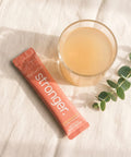 ThriveOn Stronger sachet beside a prepared golden-peach drink, morning flat-lay