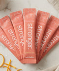 Row of 'ThriveOn Stronger' dietary supplement packets on a marble surface with orange and mango pieces.